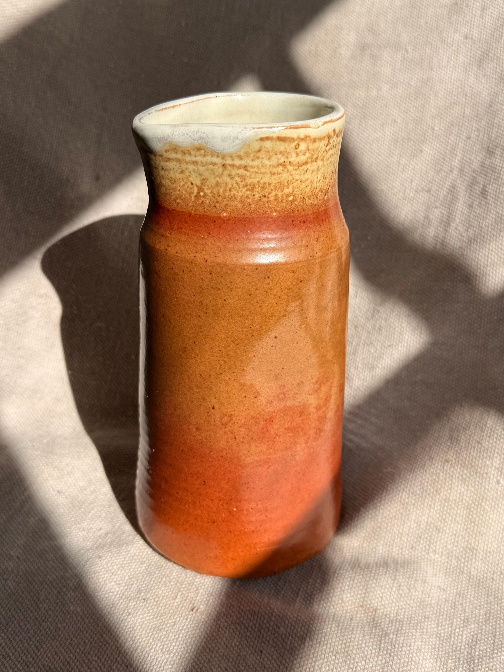 Cylindrical ceramic vase with gradient color from brown to beige on a textured surface