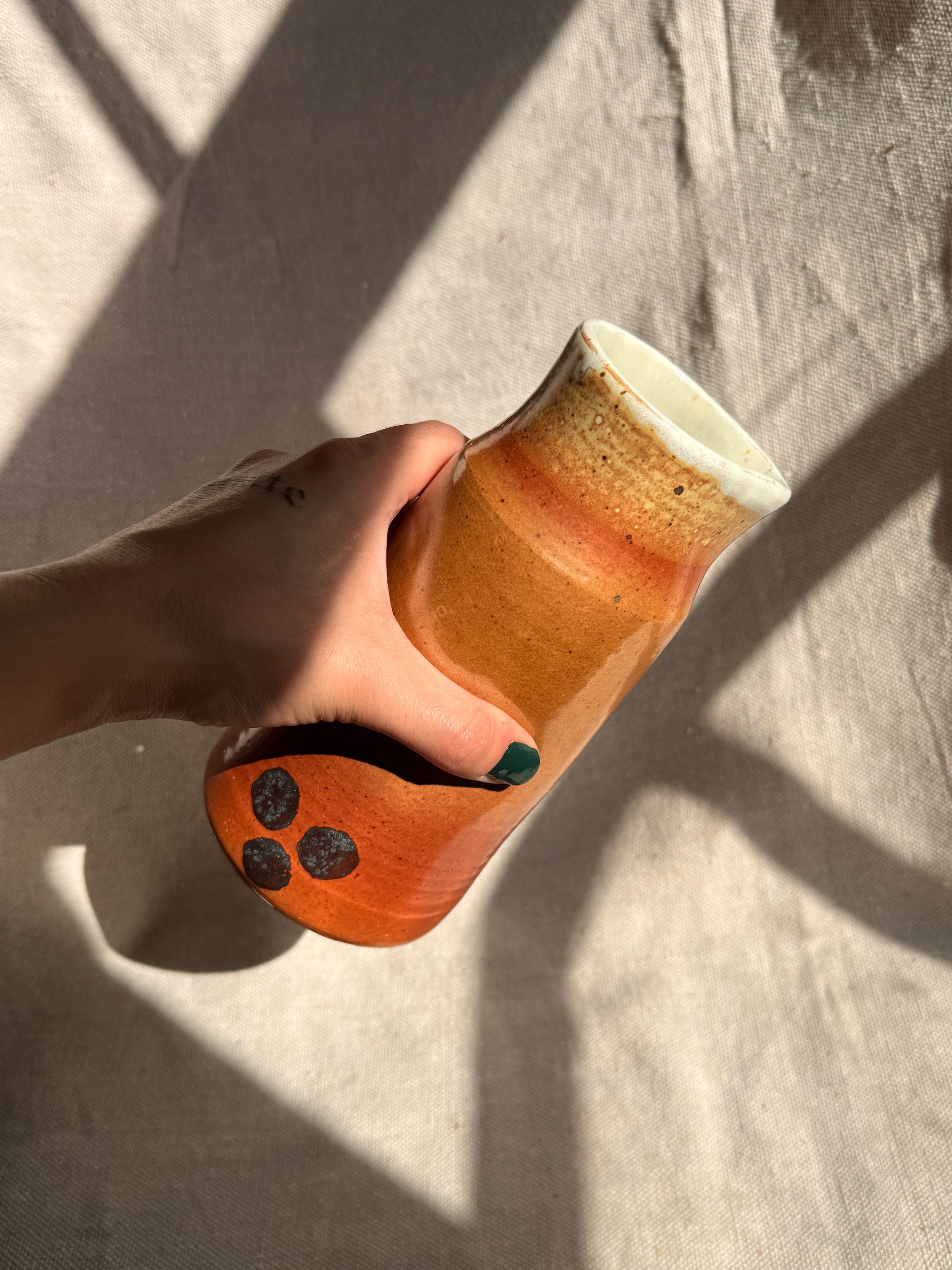 Hand holding a ceramic mug with a textured surface on a light fabric background