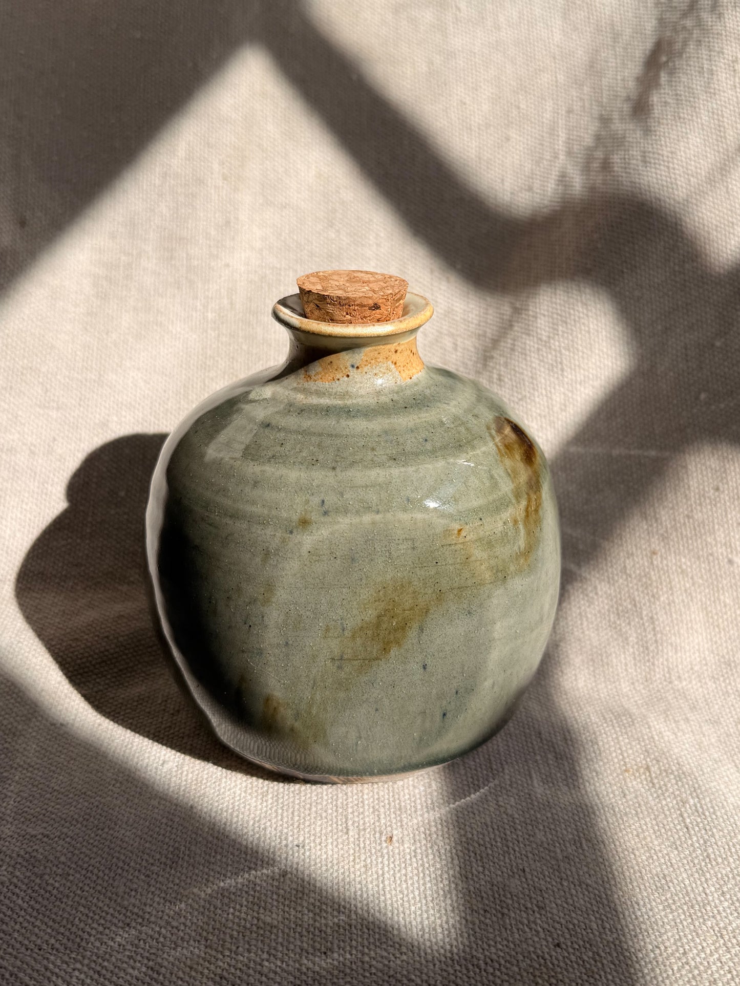 Small ceramic jar with a cork lid on a textured fabric background