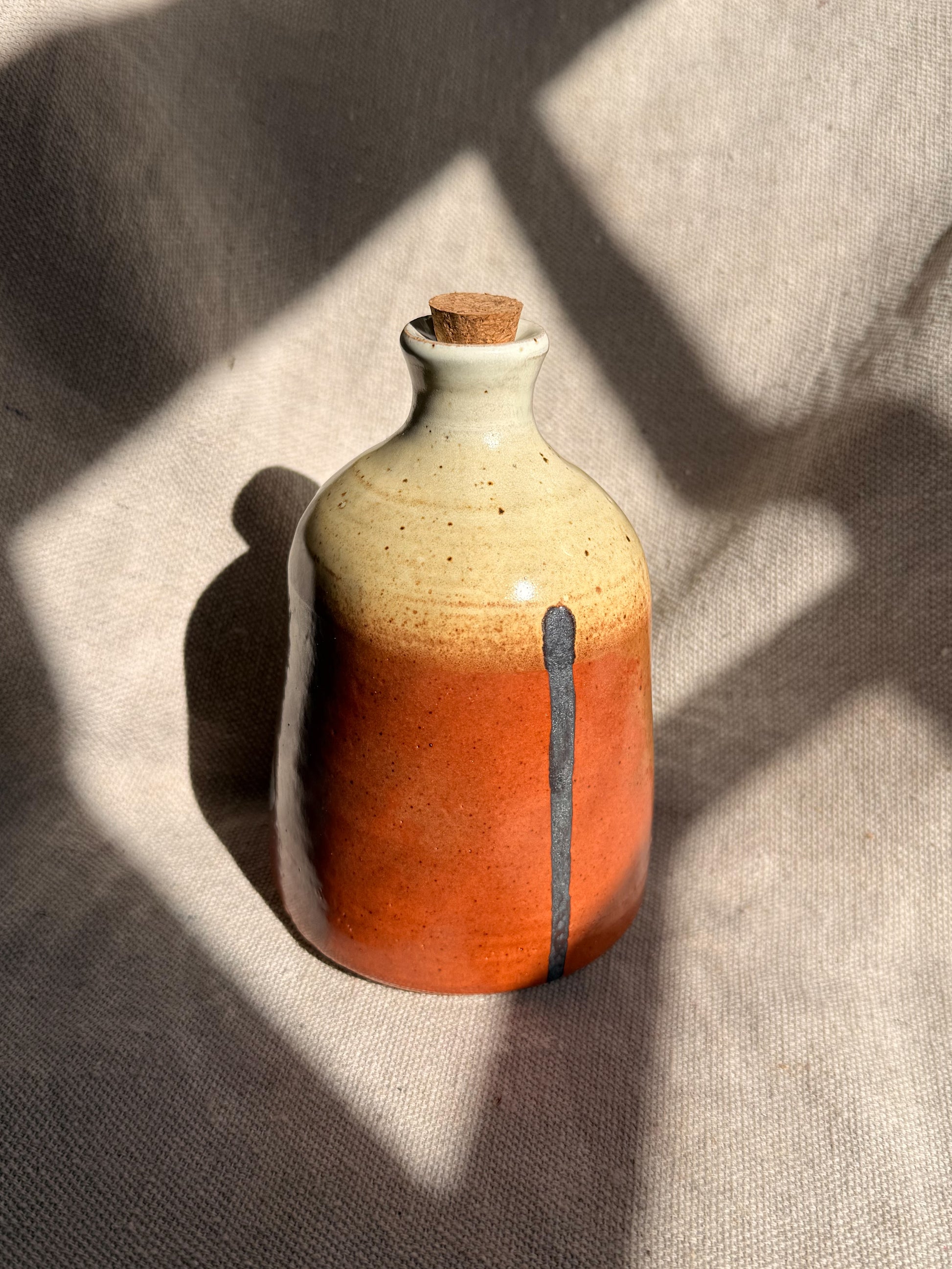 Ceramic bottle with gradient color and cork stopper on a textured fabric background