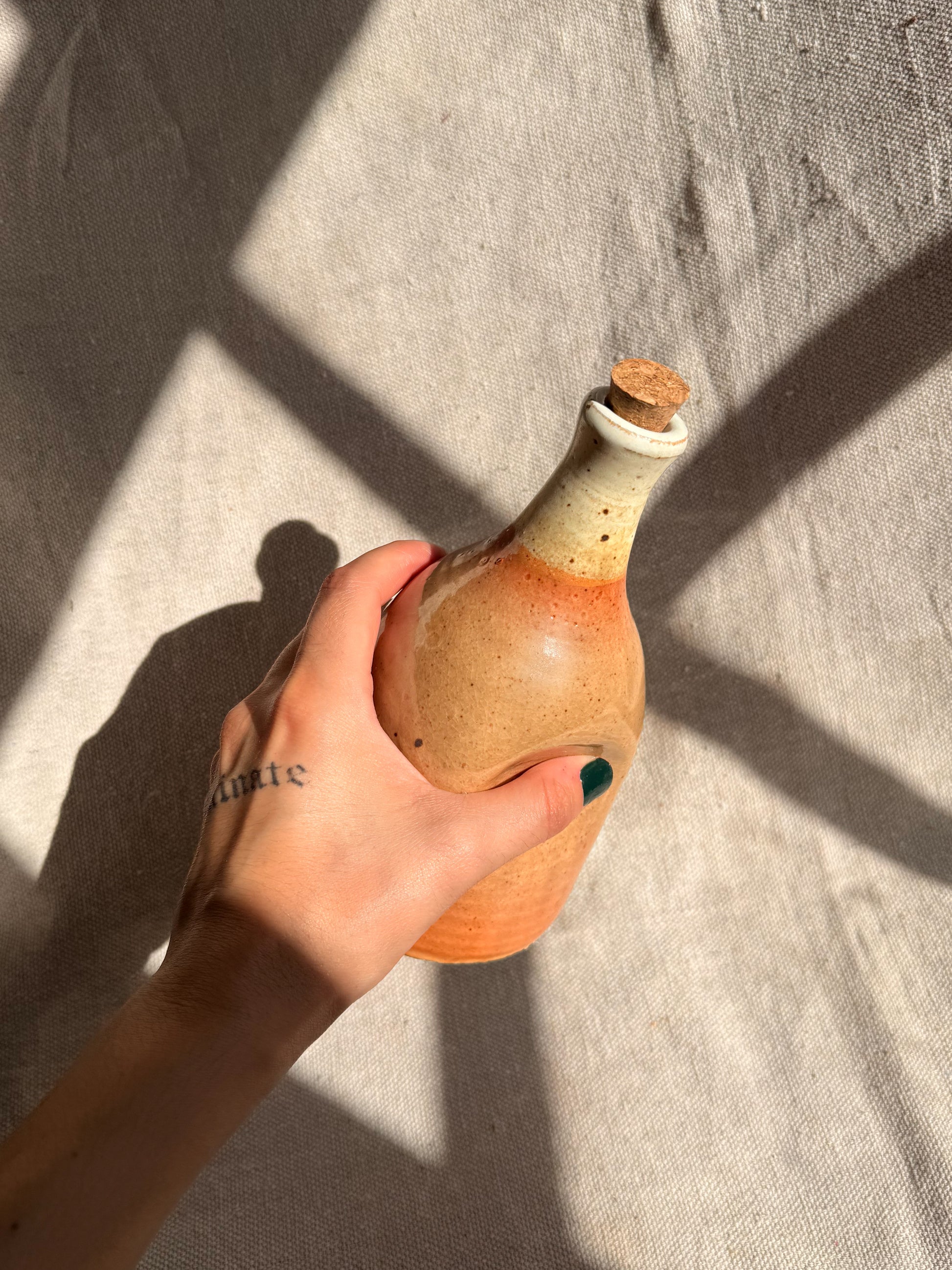 Hand holding a ceramic bottle with a cork on a textured surface