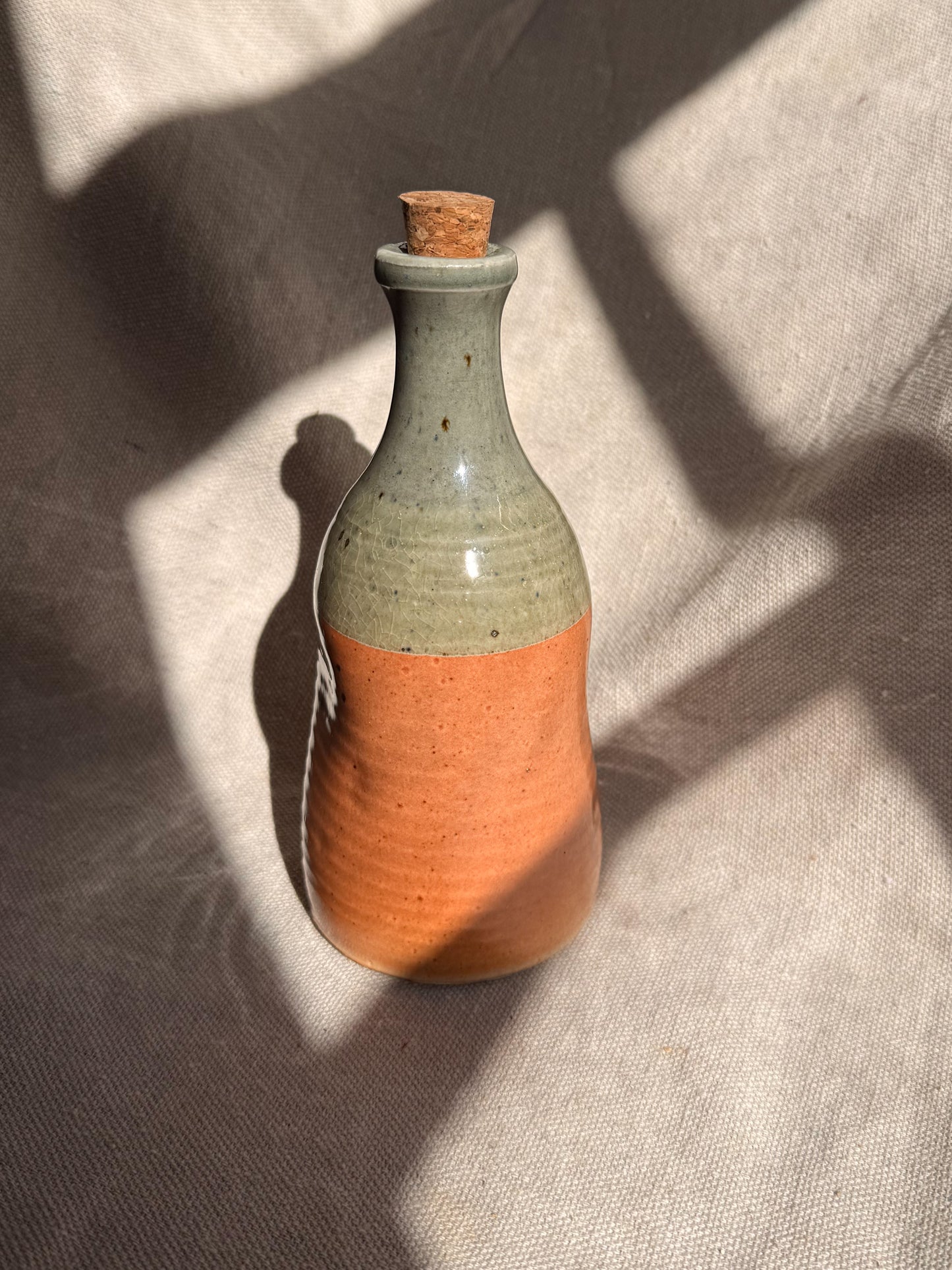 Two-toned ceramic bottle with a cork on a textured surface