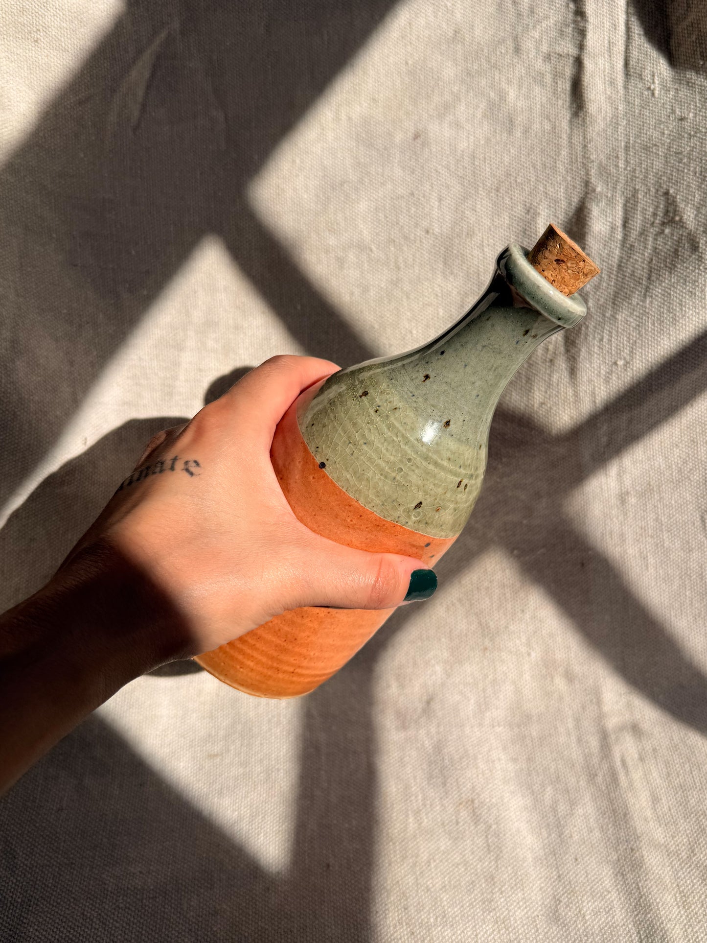 Hand holding a ceramic bottle with a textured surface against a neutral background