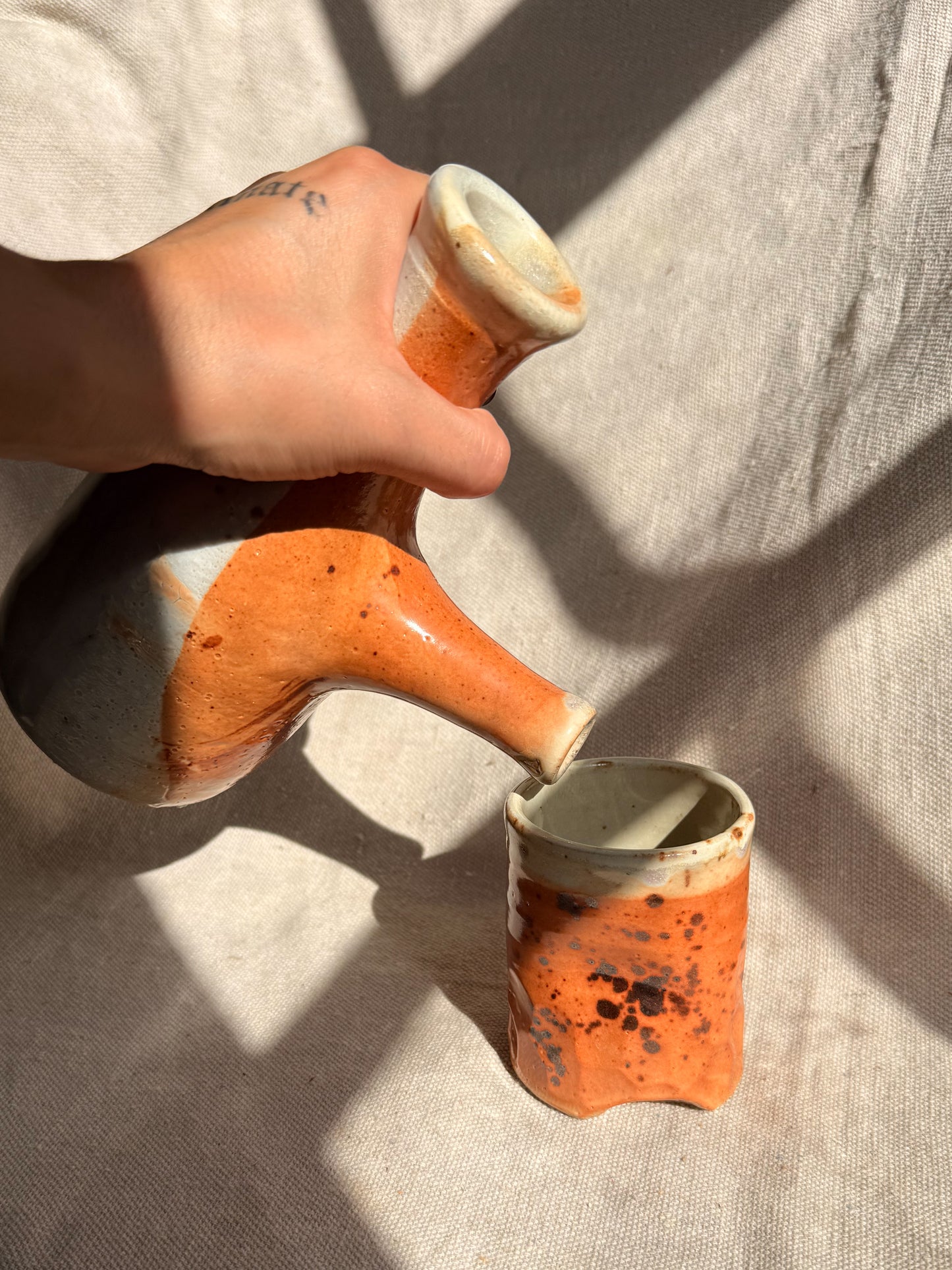 Hand holding a ceramic pipe with orange and white design on a textured surface