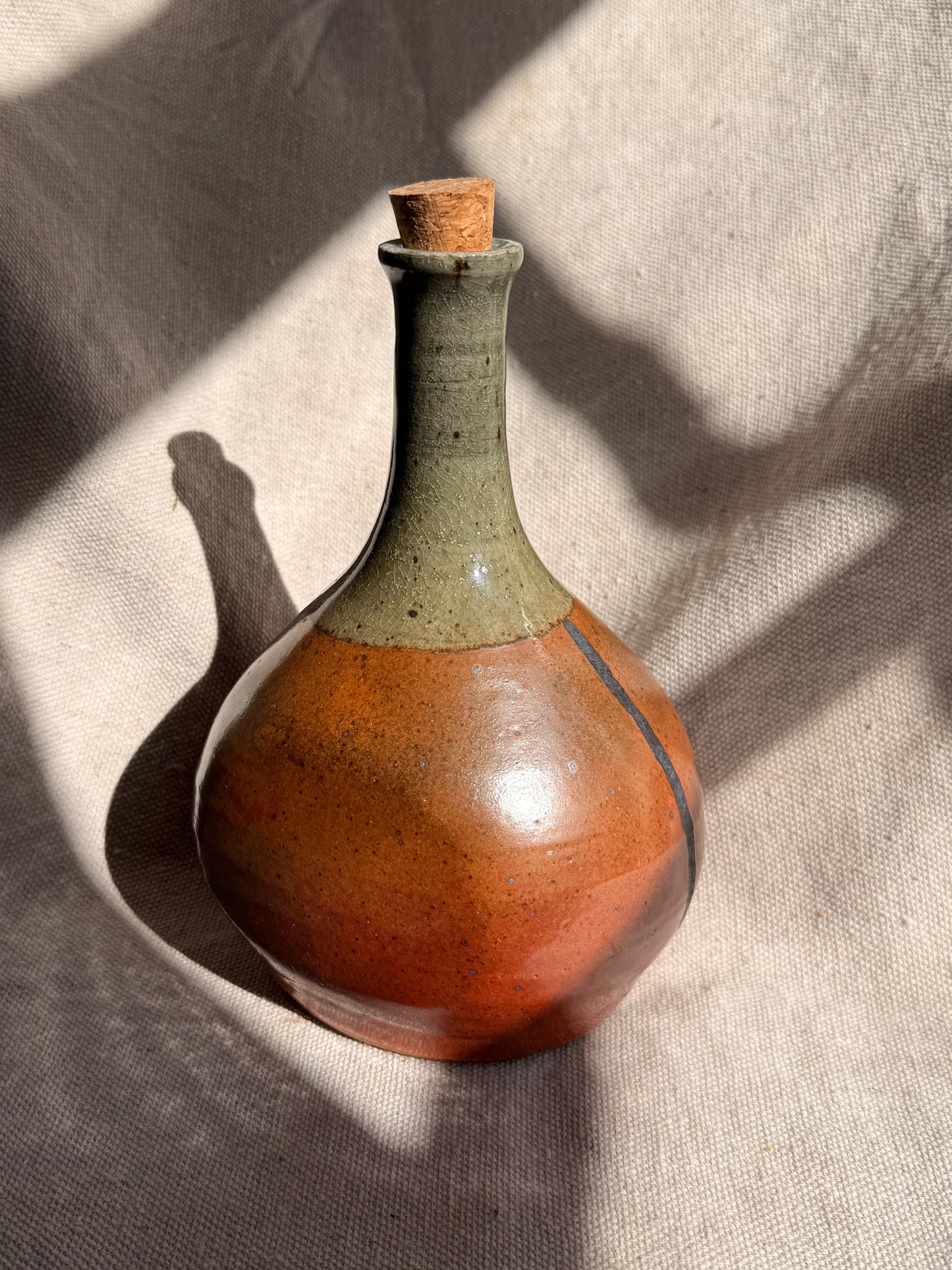 Ceramic bottle with a brown base and green neck on a textured beige surface