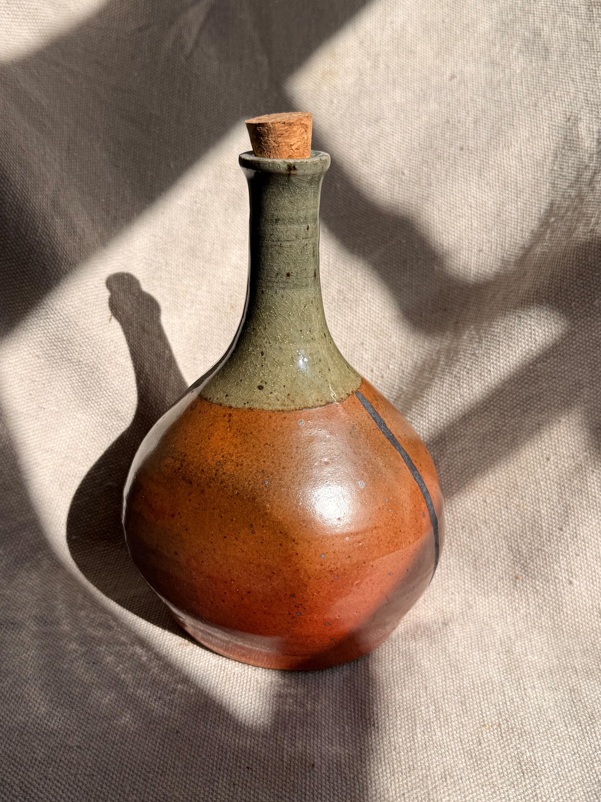 Ceramic bottle with a brown base and green neck on a textured beige surface