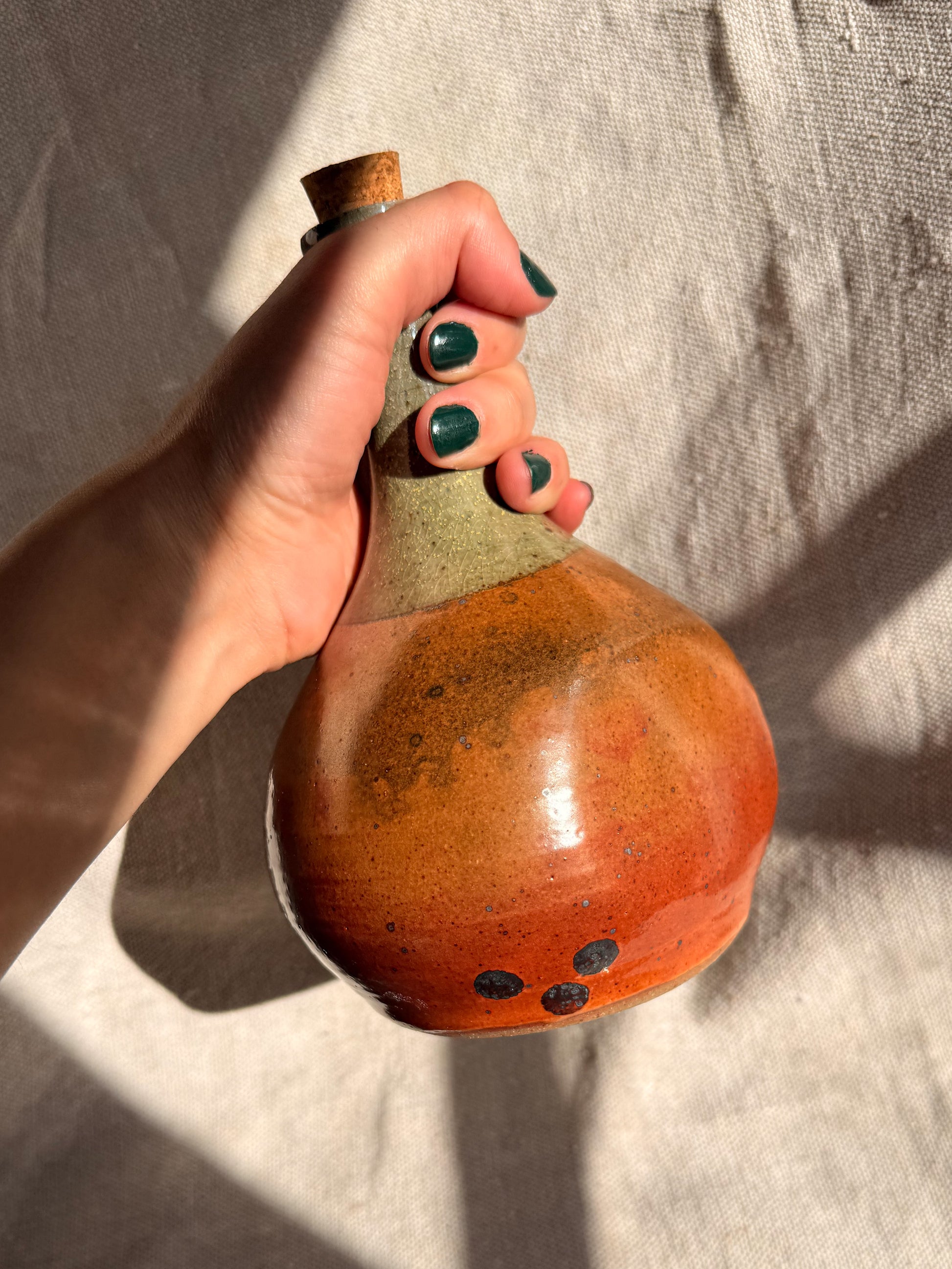 Hand holding a ceramic bottle with a textured surface against a neutral background