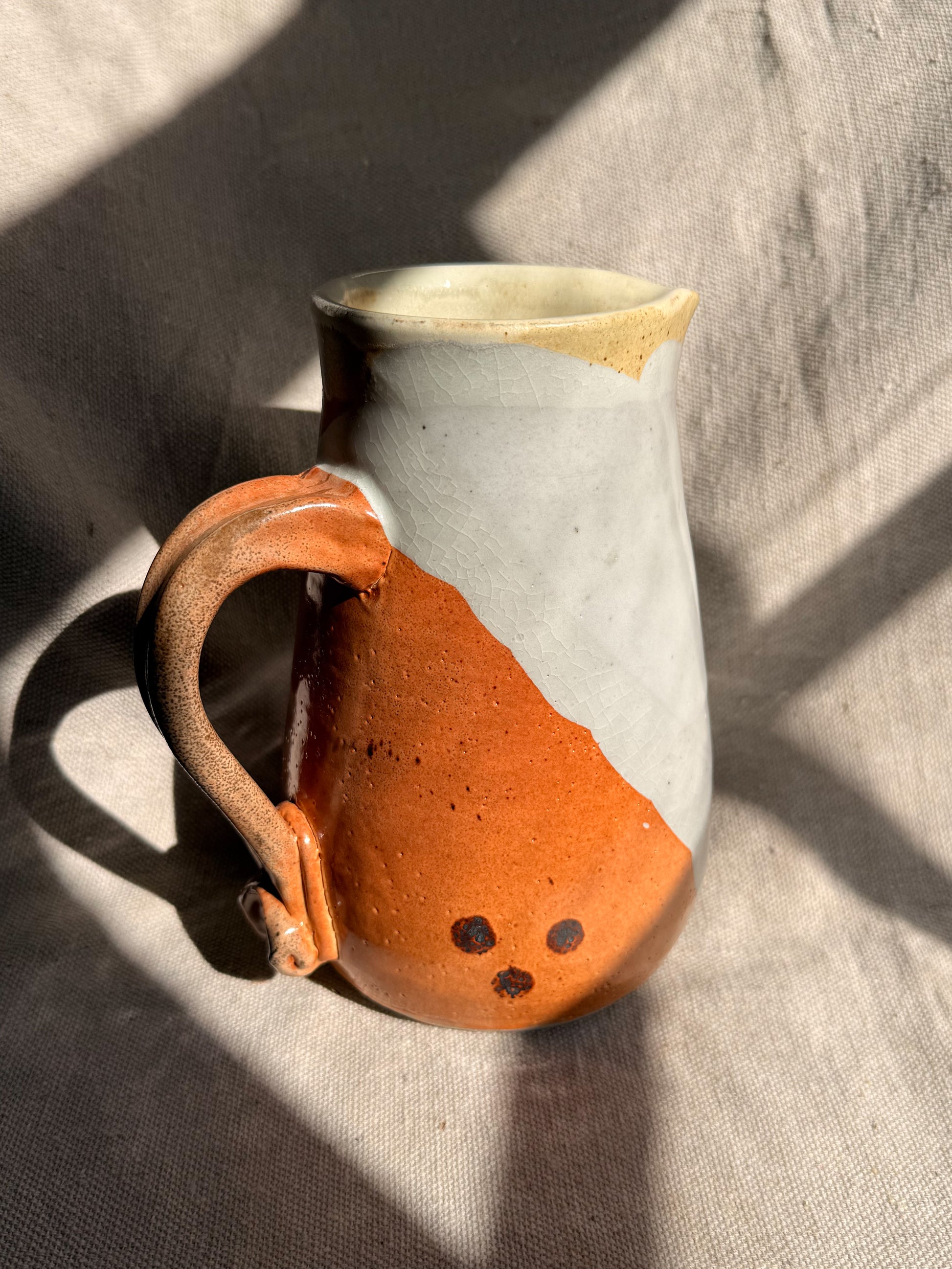 Ceramic pitcher with orange and gray design on a textured surface