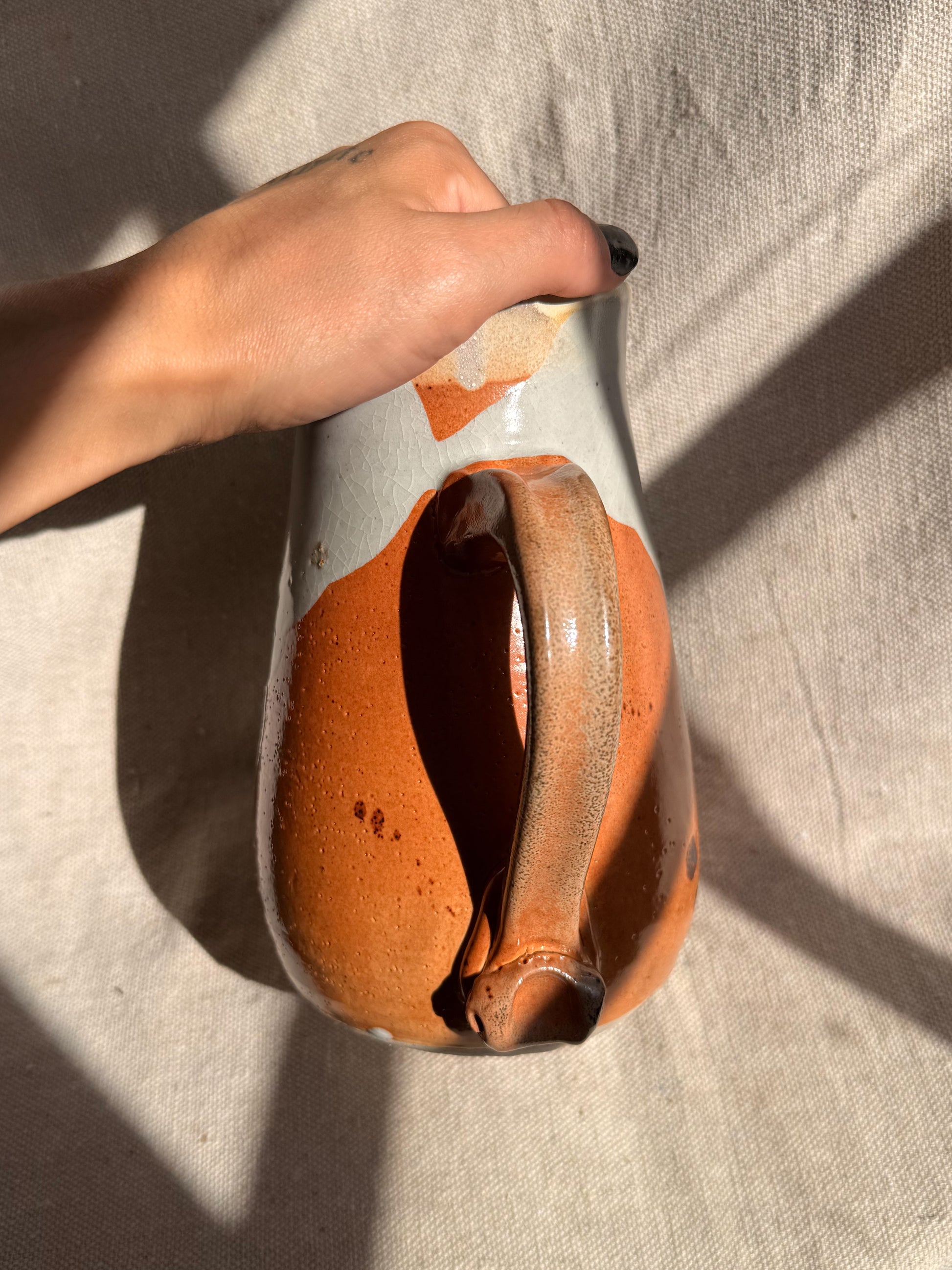 Hand holding a ceramic vase with an orange glaze against a neutral background