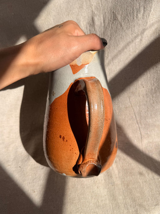 Hand holding a ceramic vase with an orange glaze against a neutral background