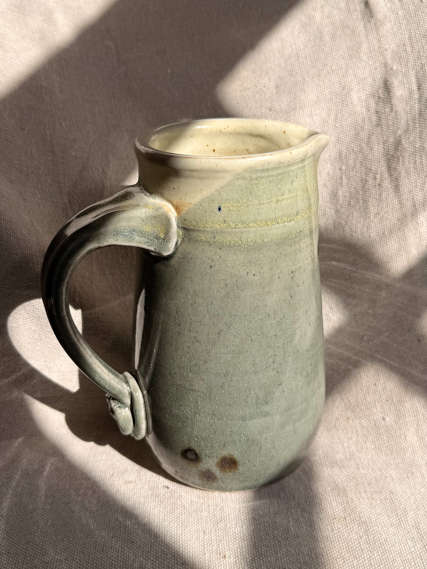 Green ceramic pitcher with a handle on a textured surface