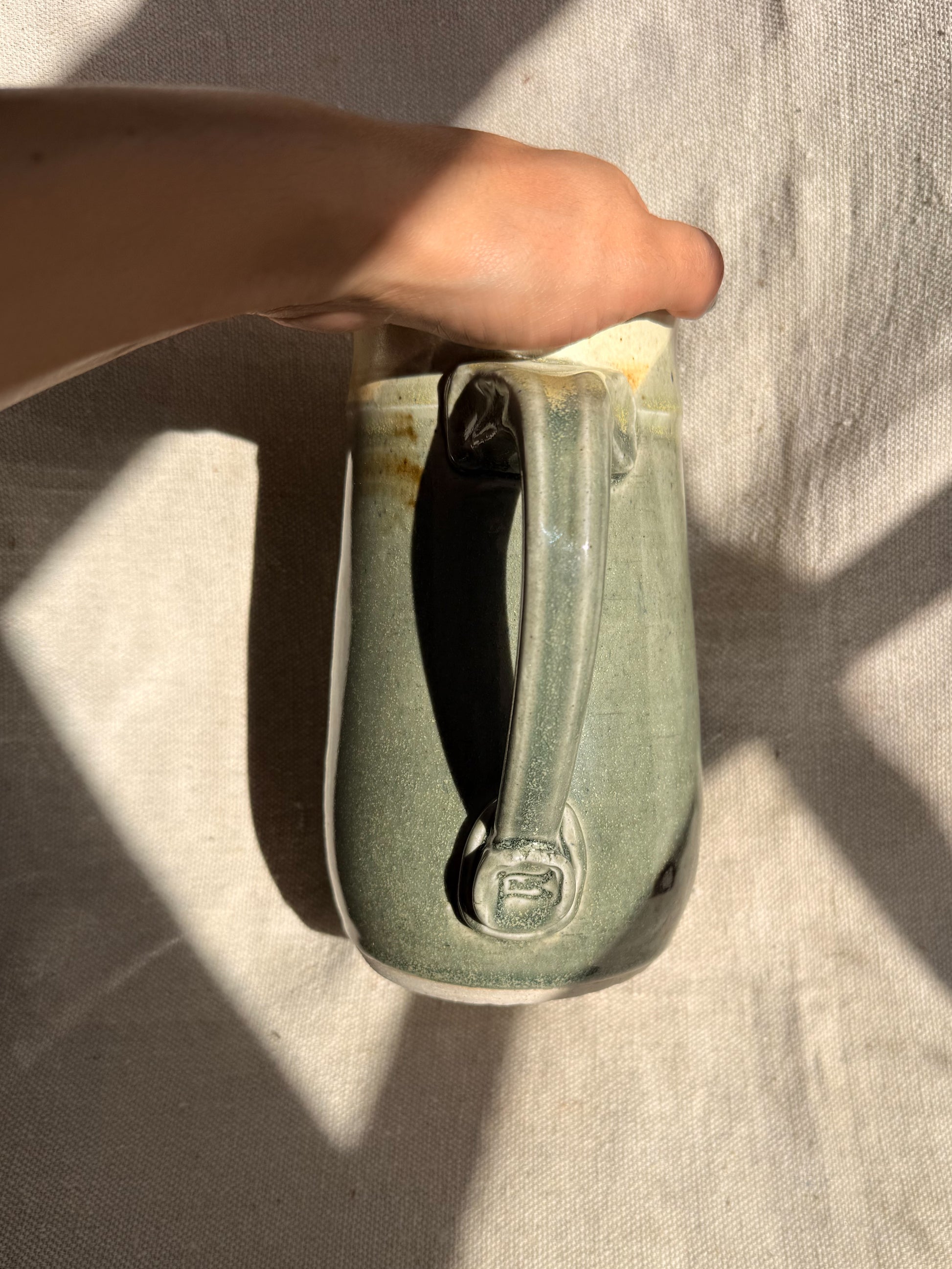 Hand holding a ceramic mug with a handle on a textured surface