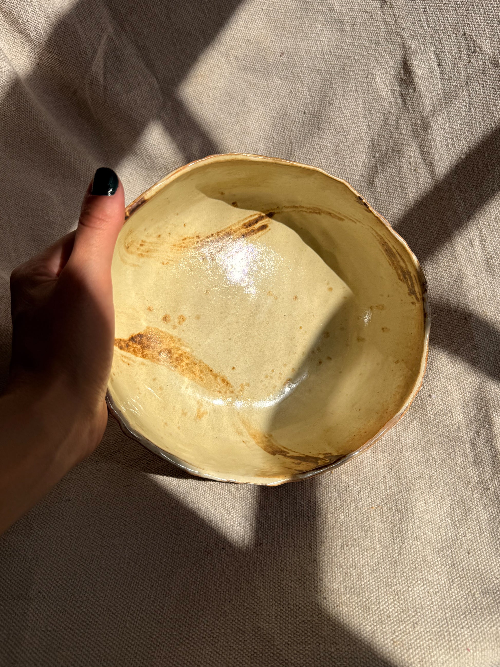 Hand holding a ceramic bowl with a textured surface on a beige fabric background