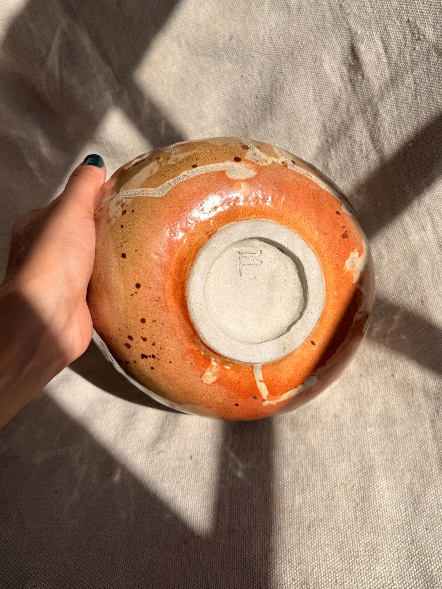 Hand holding a ceramic bowl with an orange glaze on a textured surface