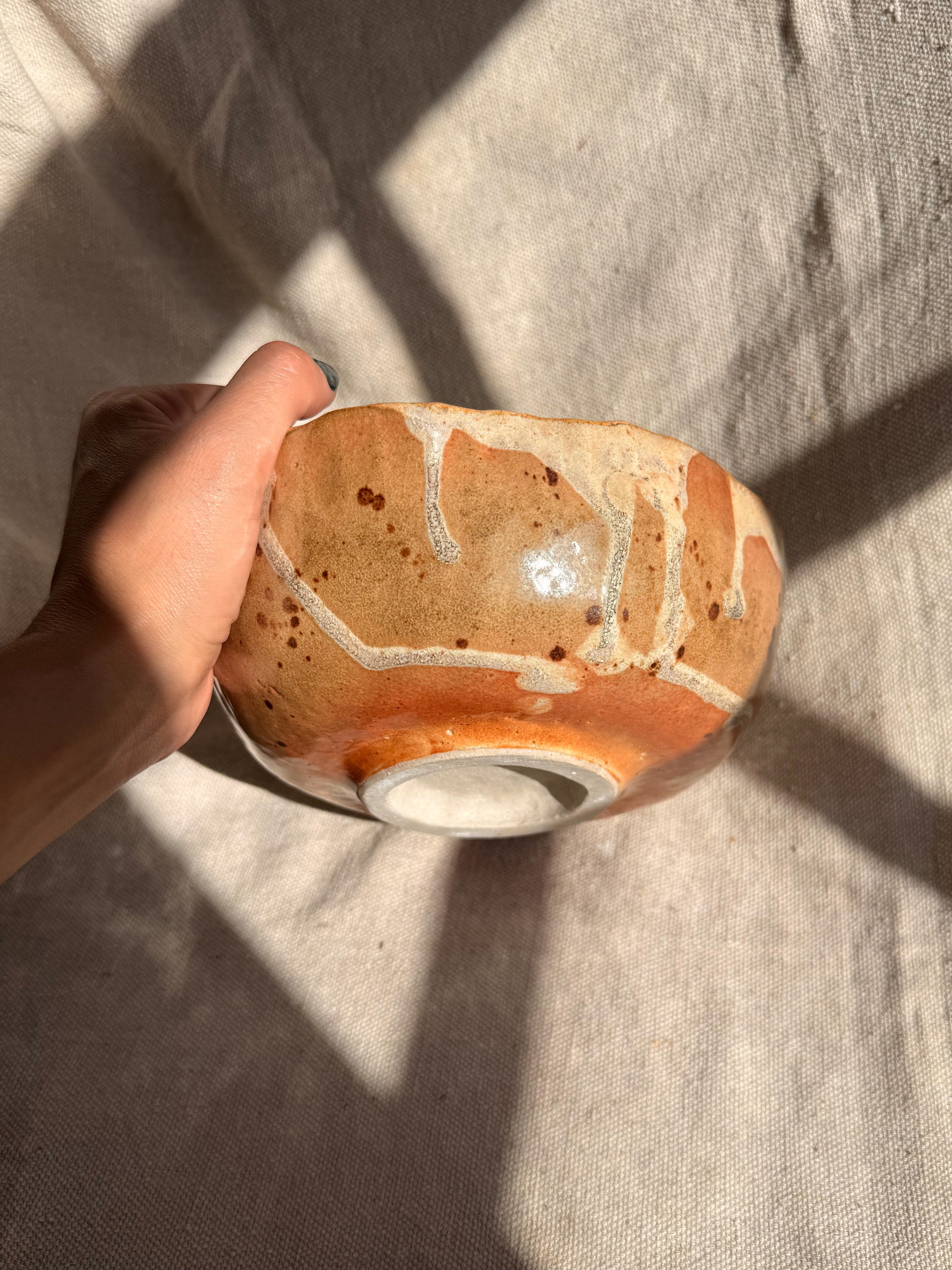 Hand holding a ceramic bowl with brown and beige glaze on a textured fabric background