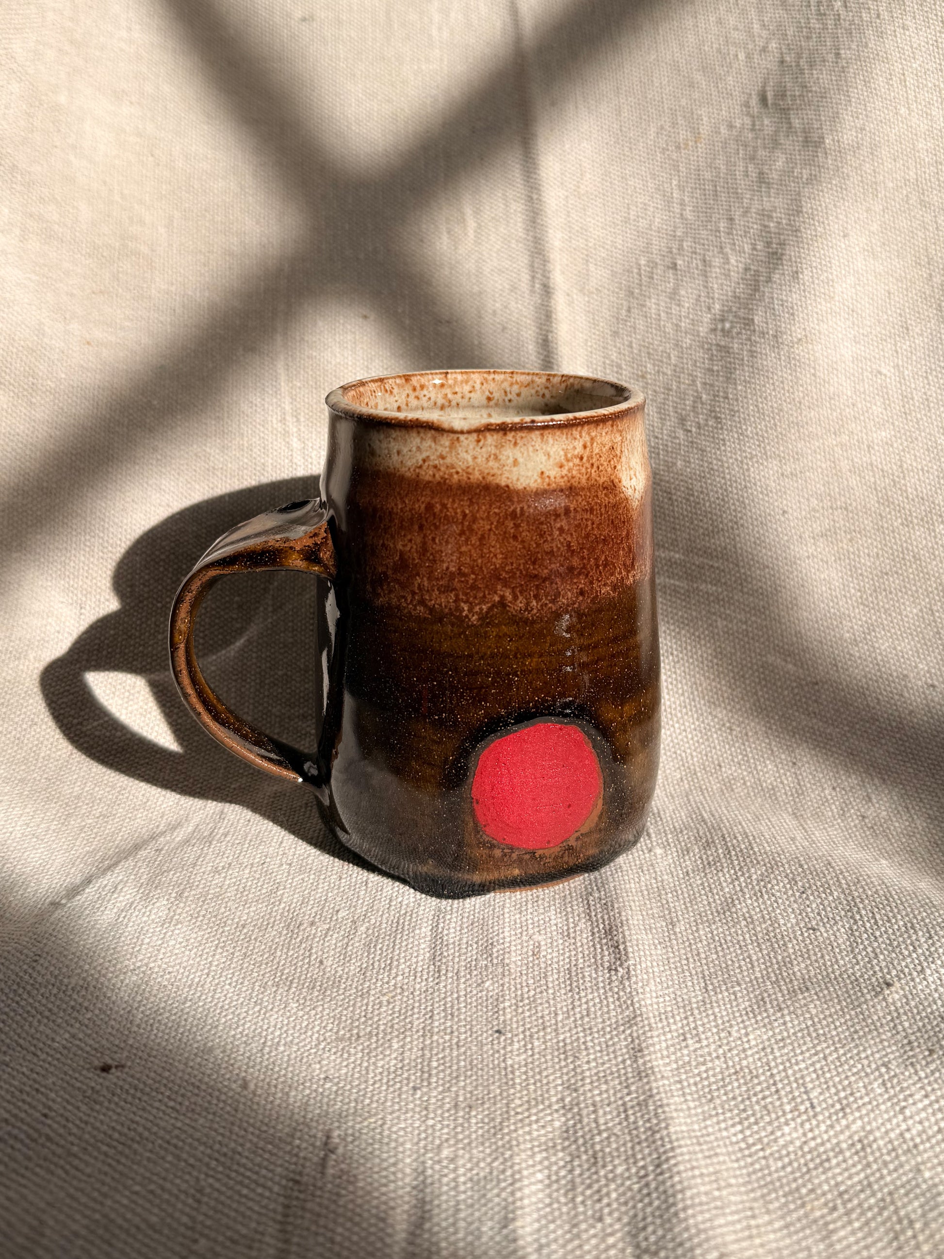 brown ceramic mug with red dot on it 