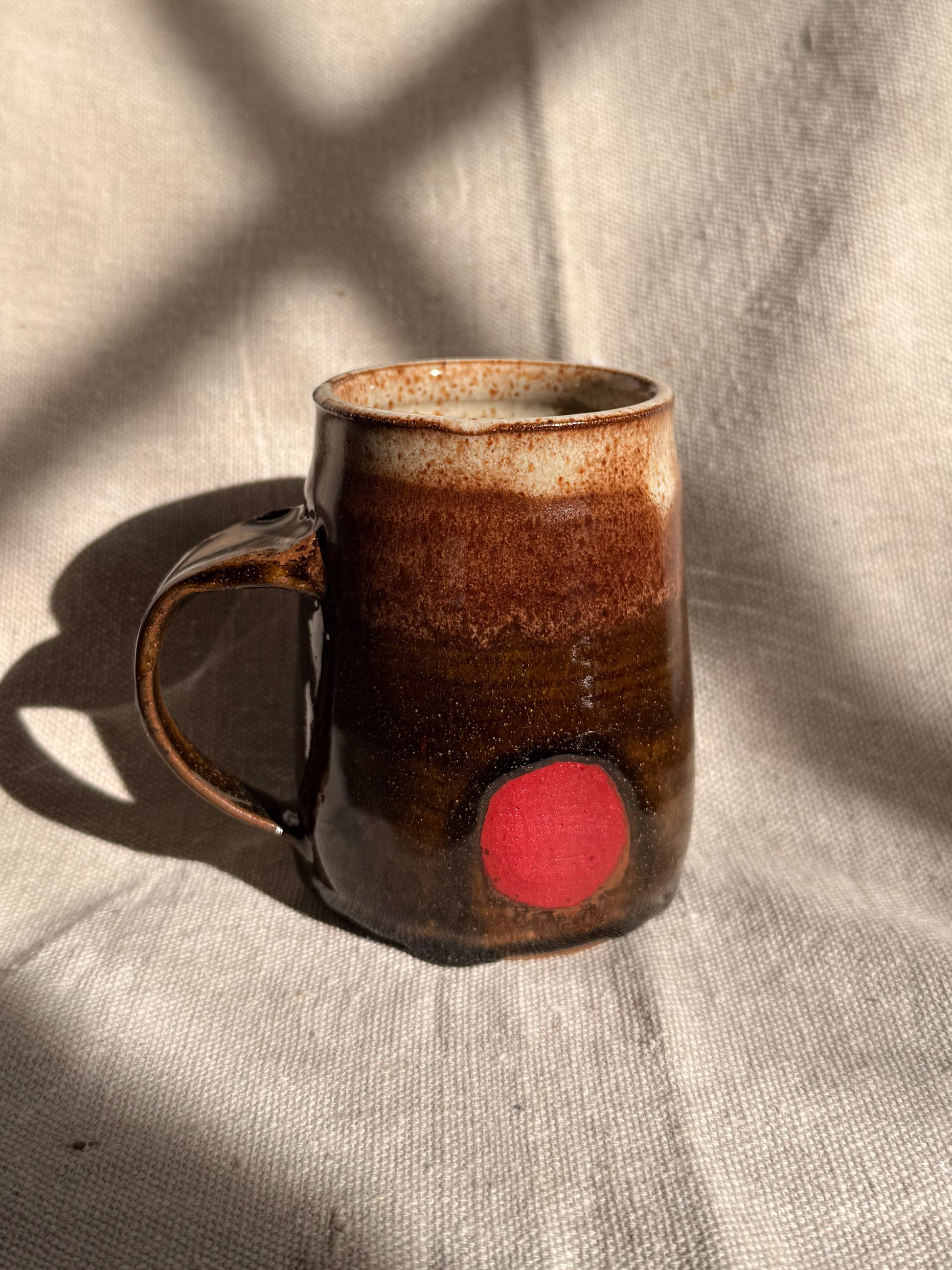 brown ceramic mug with red dot on it 