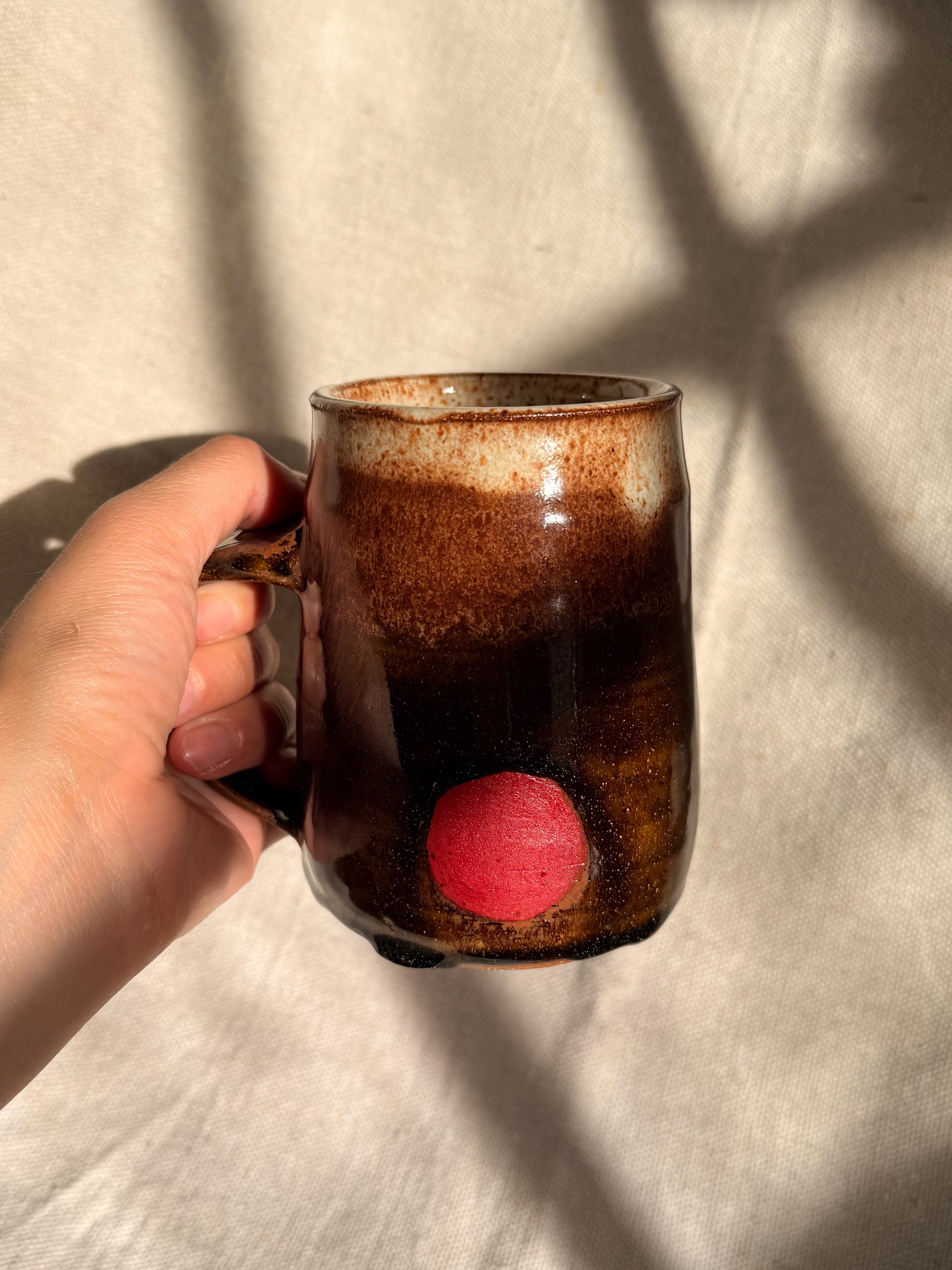 brown ceramic mug with red dot on it 