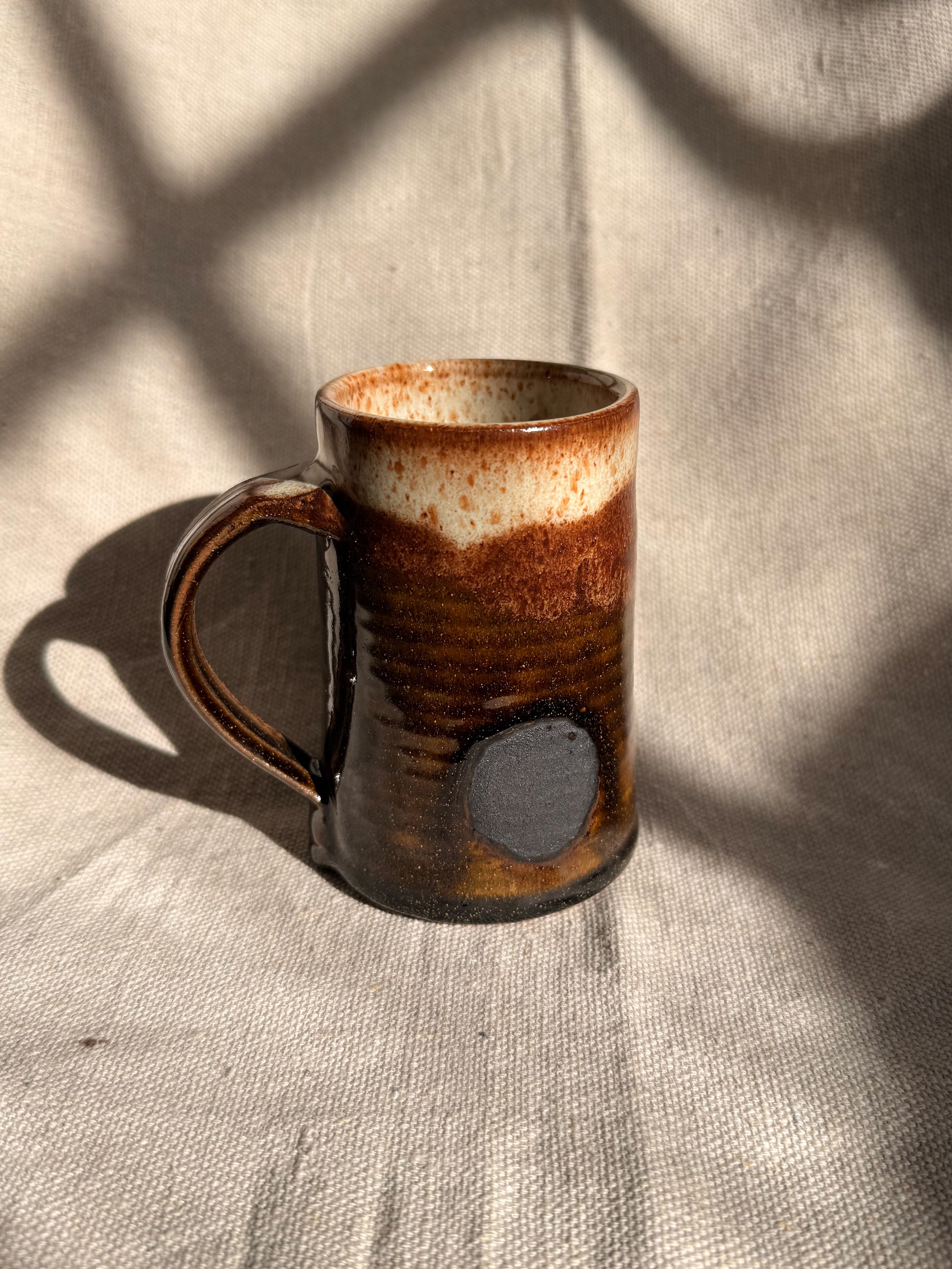brown ceramic mug with black dot on it 