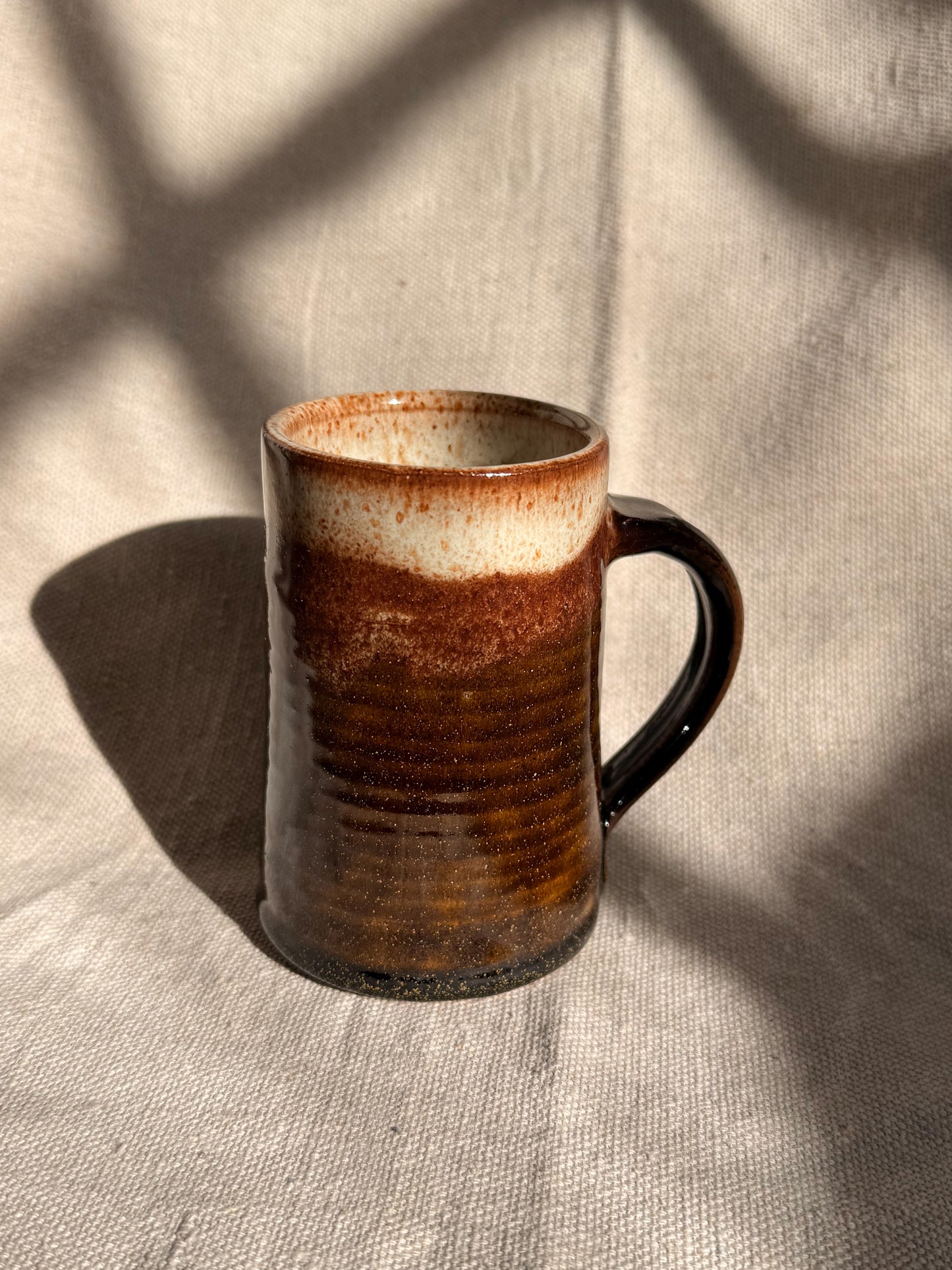 brown ceramic mug with black dot on it 