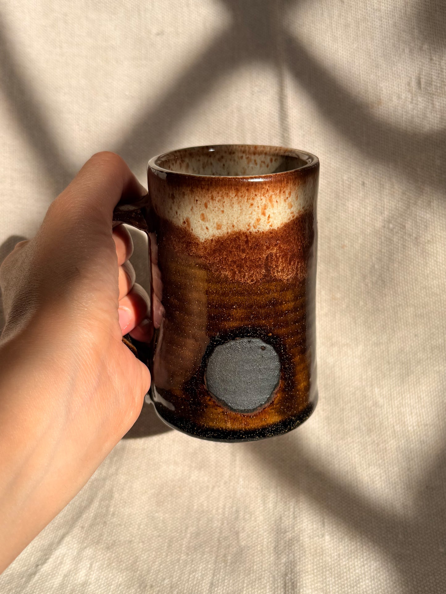 brown ceramic mug with black dot on it 
