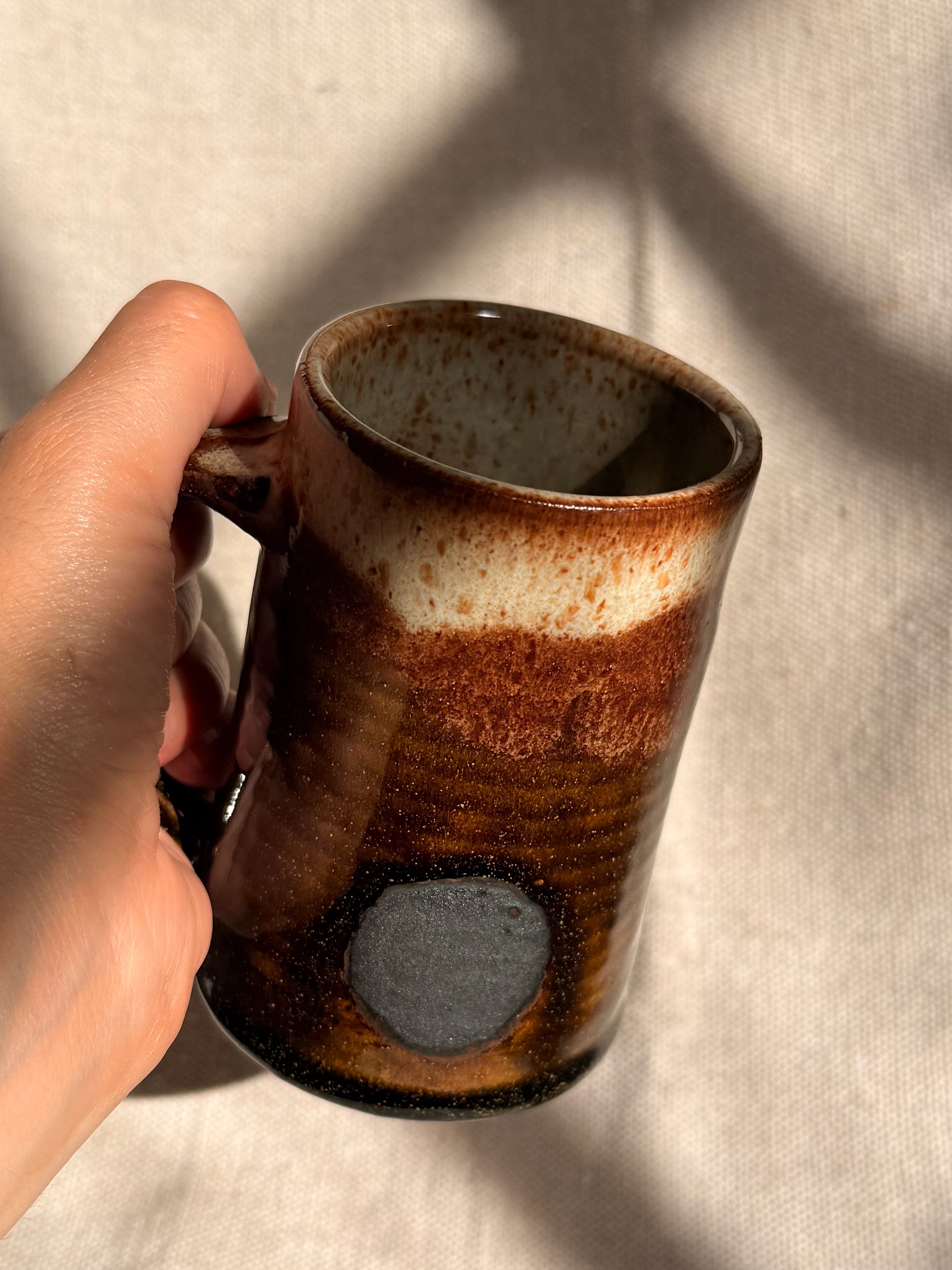 brown ceramic mug with black dot on it 